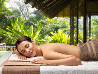 wellness, beauty and relaxation concept - young woman lying at spa over bungalow at exotic resort in thailand on background