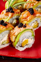 Closeup of uramaki rolls with cream cheese, mango, avocado, shrimp and black tobiko on red plate