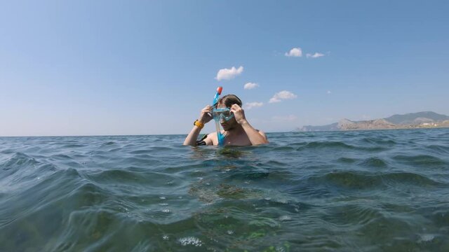 Caucasian young man preparing to dive puts on and prepares snorkeling mask while standing in the water.