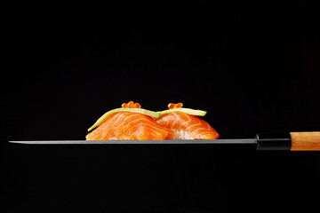 Nigiri sushi with raw salmon, avocado and red caviar on blade of Japanese knife