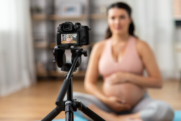 sport and people concept - close up of happy pregnant woman or blogger with camera on tripod recording online yoga class at home