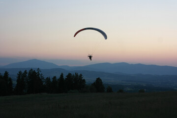 Fly paragliding adventure, flight soaring in the clouds. Freedom ambience - wind air, stunning view hill valley panorama, pink horizon gradient, aesthetics of evening mountain Tatra, Poland. 
