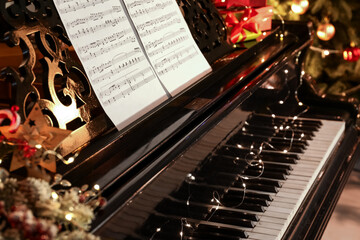 Grand piano with note sheets decorated for Christmas in room, closeup
