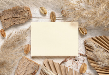 Blank card on white wooden table near dried plants, palm leaves and pampas grass