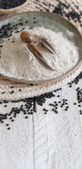 Plate with a scoop of black lentils flour and beans on white wooden table close up