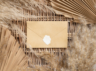 Boho sealed envelope on a wattled table with dry palm leaves and pampas grass