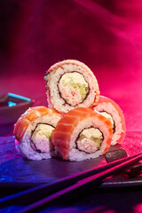 Sushi rolls served at party against multicolored background of neon lighting