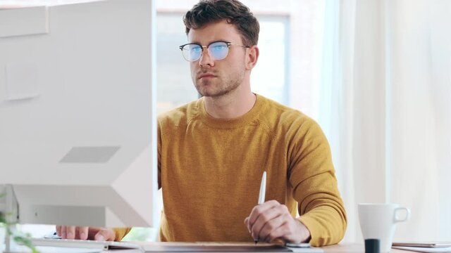 Video of graphic designer using a pen tablet while working with computer in modern startup office.