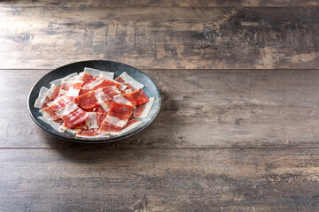 Spanish serrano ham slices on black plate on wooden table. Copy space