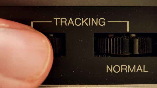Extreme close up of a button on a vintage VCR. A white finger adjusting a nob for tracking on an image making it slower.