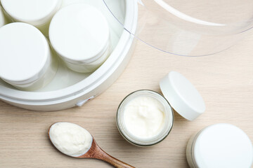 Modern yogurt maker and jars on wooden table, flat lay