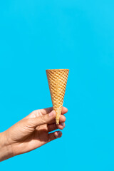 food, dessert and eating concept - close up of hand holding empty waffle ice cream cone over blue background
