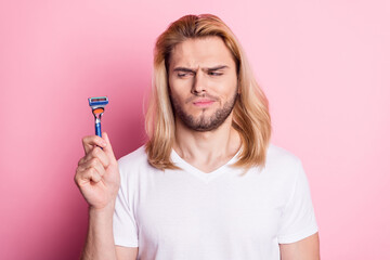Photo of unhappy upset young man look razor dislike shape skincare isolated on pastel pink color background