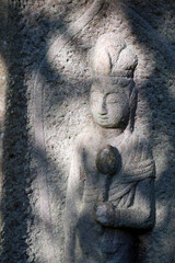 Tombstone decorated by merciful goddess stone sculpture. 山の中にひっそりと安置されている墓石に彫られた異国風の菩薩像。日差しを柔らかく受けている写真。