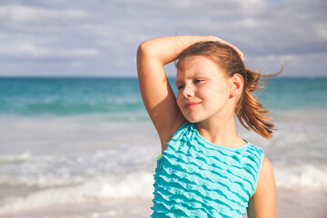 Fototapeta na wymiar Pretty little girl in blue dress stands on an ocean coast