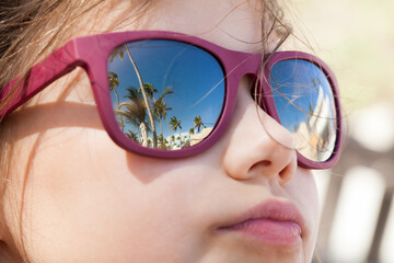 Little girl in a sunglasses with reflections of tropical beach
