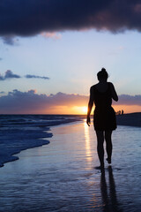 Silhouette photo of a girl walking on ocean coast under sunrise sky