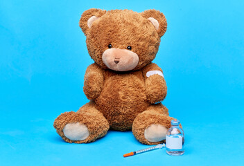 vaccination, healthcare and pandemic concept - teddy bear toy with patch on paw, vaccine and syringe over blue background