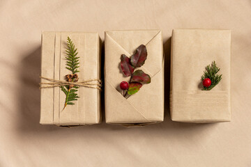 Three Christmas gift boxes, eco-friendly wrapping style. Craft brown paper with trendy folds and natural twigs on linen textile background