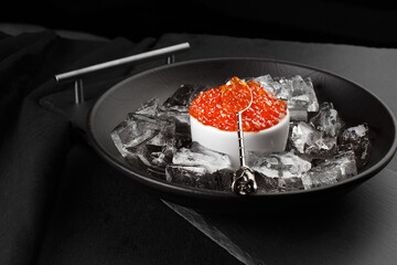 Red caviar in a bowl with ice and a glass of champagne on a tray. Christmas and New Year background