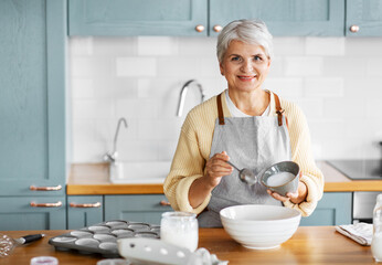people and culinary concept - happy smiling woman cooking food on kitchen at home and adding sugar