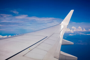 Plane window view with blue sky and clouds.