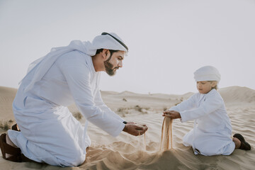 Father and son spending time in the desert on a safari day. Arabian family from the emirates wearing the traditional white dress. Concept about lifestyle and middle eastern cultures
