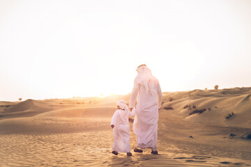 Father and son spending time in the desert on a safari day. Arabian family from the emirates wearing the traditional white dress. Concept about lifestyle and middle eastern cultures - obrazy, fototapety, plakaty