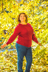 Chubby sunny woman in warm casual clothes in city park. Clothes for plus size ladies