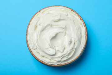 Bowl of tasty cream cheese on light blue background, top view