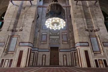 Old decorated bricks stone wall with colored marble decorations, big brass chandelier, and ornate wooden door in al Refai mosque, Cairo, Egypt