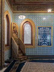 Wooden golden ornate minbar (Platform),  wooden arched window framed by golden ornate floral pattern, and ceramic tiles wall with floral blue patterns