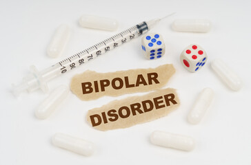 On a white surface lies a syringe, pills, dice and pieces of paper with the inscription - BIPOLAR DISORDER