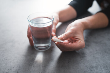 Human hand holding a pills and glass of water. Detail of hand with medicine. Concept of medicine, daily routine and pharmacy.