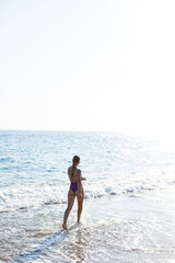 Fototapeta na wymiar A young beautiful woman with a toned body in a bright swimsuit walks along the sandy beach. Summer vacation at the sea. Mediterranean Turkish Sea. Selective focus