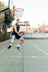 Man jumping with a ball in front of a basket in an outdoor court