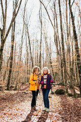 Fototapeta premium Two senior female friends hiking together through the forest in autumn