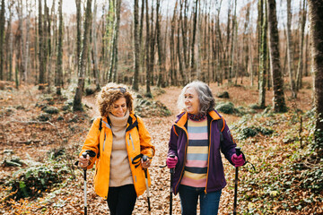 Two senior female friends hiking together through the forest in autumn