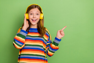 Portrait of beautiful trendy cheerful amazed girl listening pop showing copy space ad isolated over bright green color background