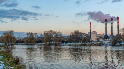 Fototapeta premium Smoking chimneys of thermal power plants near the waterfront in city. Winter. Industrial and nature background.