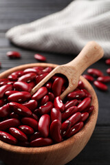 Raw red kidney beans in bowl and scoop on dark wooden table, closeup