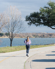 Rear view Caucasian lady with headphone running on sidewalk near White Rock Lake park in Dallas, Texas, USA