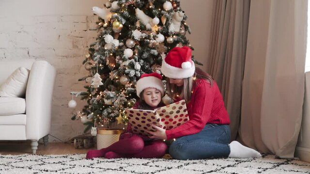 Beautiful mother reading a book of fairytales for her cute small daugter