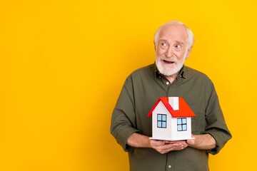 Photo of minded dreamy person hold small house look empty space isolated on yellow color background