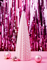 Concept is modern decor for Christmas. Small ceramic pink Christmas tree on background of tinsel and flying paper confetti. Festive mood