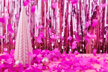 Concept is modern decor for Christmas. Small ceramic pink Christmas tree on background of tinsel and flying paper confetti. Festive mood. Copy space