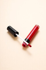 Open tube red lipstick and applicator wand on beige background. Makeup cosmetic product