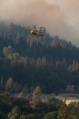 Breathtaking shot of a helicopter flying over a burning forest trying to extinguish the fire © Shphoto908/Wirestock