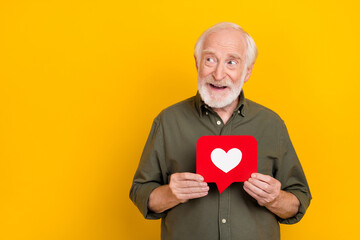 Photo of positive aged man hold like comment card look interested empty space isolated on yellow...