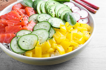 Delicious poke bowl with salmon and vegetables on wooden table, closeup